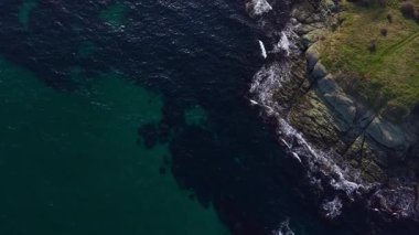 Canlı mavi sular bu büyüleyici kıyı sahnesinde karanlık kayalık kıyılarla buluşur. Yumuşak dalgalar, temiz gökyüzünün altındaki toprağı okşar doğanın saf güzelliğini gözler önüne serer..