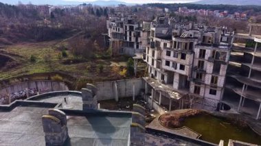 Yapılar, bir zamanlar yoğun olan bir gelişmede sessiz kalıyor, şimdi ise, doğa yavaş yavaş toprağını geri kazanırken, unutulmuş rüyaları hatırlatan ve potansiyelini yitirmiş bir çadır bezi..