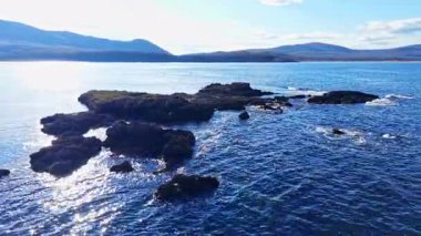 Işıl ışıl bir gökyüzünün altında, sakin sulardan kayalık çıkıntılar ortaya çıkar, keşifleri davet eder. Hafif dalgalar kıyıya vururken uzak tepeler güneş ışığıyla yıkanır..