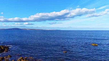 Dalgalar yavaşça kayalık oluşumlara doğru süzülüyor bulutlar tembelce üzerlerinde sürükleniyor, bu sakin sahil cennetinde suyun kenarında doğanın güzelliğini resmediyor..