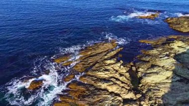 Sert kaya oluşumları derin mavi denizden çıkar. Yumuşak dalgalar kenarlarına çarpar. Güneş ufkun aşağısında, doğanın sahil şeridinin güzelliğini artırmak için sahnenin üzerine ılık bir parıltı saçar..