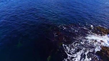 Parlak güneş, dalgaların engebeli kayaları öptüğü sakin bir okyanusun üzerinde parıldıyor. Sahne huzuru ve doğanın güzelliğiyle bağlantıyı davet eder..