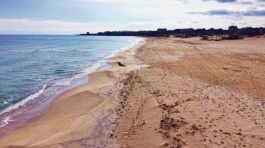 Sahil şeridi boyunca uzanan altın kumlar sakin bir sabah sırasında sakin mavi sularla usulca karşılaşıyor. Ayak izleri uzak sahil kulübelerine gidiyor. Sıcak bir günü işaret ediyor..