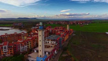 Renkli binalar ve uzun bir deniz feneriyle denize bakan pitoresk bir köy. Gün batımında güzel bir gökyüzünün altında yemyeşil tarlalar uzanıyor..