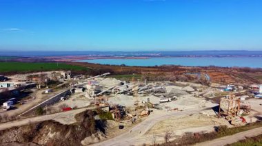 Ağır makineler, güneşli bir günde doğa ve sanayinin yan yana gelişini gösteren barışçıl bir gölün yanındaki çakıl taşlı çıkartma sahasında verimli bir şekilde çalışır..