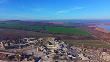 Meşgul işçiler, parlak mavi gökyüzüne karşı kurulu büyük bir sitede, canlı yeşil alanlar ve arka planda çarpıcı bir kontrastlık yaratan sakin bir göl ile inşaat faaliyetlerinde bulunuyorlar..