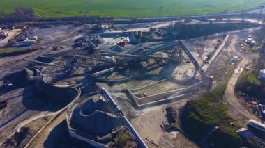 Yukarıdan görülebilen, yoğun inşaat sahasında işçiler canlı, endüstriyel bir arazide malzeme akışını verimli bir şekilde yönetirken kamyonlar, taşıyıcılar ve çakıl yığınları yer alıyor..