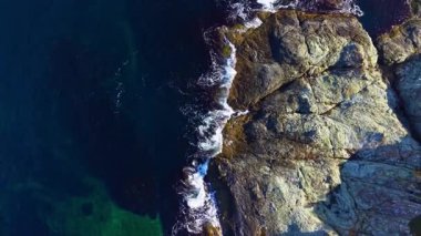 Parlak güneş ışığı derin mavi denizde dans eder, yumuşak dalgaların engebeli kayalarla buluştuğu yerde, berrak bir gökyüzünün altında doğanın güzelliğini barışçıl bir şekilde görme imkanı sunar..