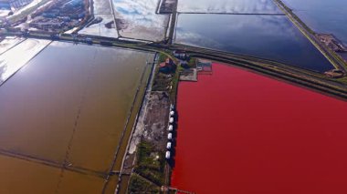 Parlak kırmızı, mavi ve kahverengi tuz tavaları, sakin bir günbatımında suyun gökyüzünün renklerini yansıttığı olağanüstü bir görsel manzara yaratır. Doğanın büyüleyici bir paleti gözler önüne seriliyor..
