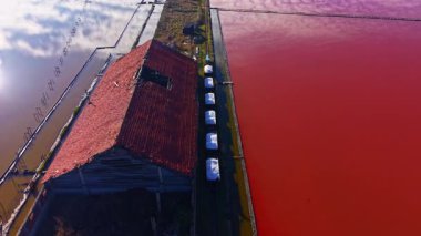 Renkli tuz düzlükleri manzara boyunca uzanıyor, yan yana gelen canlı kırmızı ve sakin mavi renkler, eski bir binanın kalıntıları sahneye cazibe katıyor..