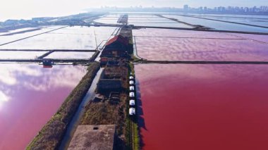 Uçsuz bucaksız bir tuz tabakasının çarpıcı görüntüsü açık bir gökyüzünün altında canlı kırmızı ve pembe renklerde parlıyor. Su parıldayan güneş ışığını yansıtırken terk edilmiş yapılar unutulmuş hikayelere işaret ediyor..