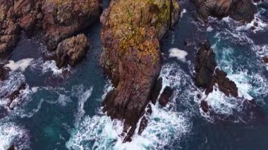 Turkuaz sular aşınmış kayalıkların etrafında dalgalanarak kayalık kıyı şeridine karşı çarpıcı bir kontrastlık yaratır. Güneş ışığı bu sakin kıyı sahnesinde dalgalarda parıldıyor..