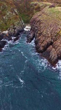 Dalgalar engebeli uçurumlara çarpıyor güneş parlak mavi sularda parlarken. Yeşil bitki örtüsü kayalık araziye hayat katıyor, nefes kesici bir kıyı manzarası yaratıyor..