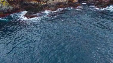 Sabahın erken saatlerinde okyanusta hafif dalgalar engebeli kayalarla buluşurken ışık dans eder. Sahne huzurlu, sahil şeridi boyunca doğanın güzelliğini yansıtıyor..