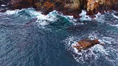 Güneş ışığı su yüzeyinde parıldıyor dalgalar yükselen uçurumlara çarparak gün batımında huzurlu bir kıyı şeridinde köpük ve sıçrama yaratıyor..