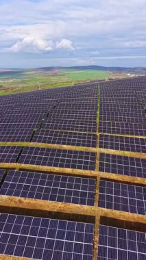 Sahne, geniş bir alana yayılan güneş panellerini gösteriyor. Konumda yeşil alanlar ve bulutlu mavi bir gökyüzü yer alıyor. Yenilenebilir enerji bu ortamdaki ana odak noktasıdır..