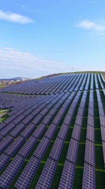 Güneş panelleri bir yamacı kaplıyor. Güneş batıyor, yeşil çimlere ve mavi gökyüzüne karşı panelleri parlaklaştırıyor. Ayarlar sürdürülebilir bir enerji kaynağı gösteriyor.