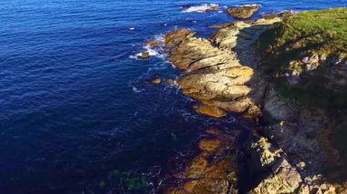 Dalgalar yavaşça sarkık kayalara çarpar, güneş ışığı tarafından öpülürler ama yumuşak yeşillikler ve altınlarla gölgelenirler. Ufuk genişçe uzanıyor, doğa aşıkları için huzurlu bir kaçış yaratıyor..