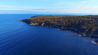 Sakin okyanusun üzerinde yemyeşil sularla çevrili görkemli uçurumlar yükselir. Yumuşak dalgalar kıyı şeridini öperken öğleden sonra güneşi sakin sahnenin üzerine sıcak bir ışık saçıyor..