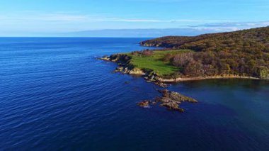 Güneş sakin bir sahil şeridinde yükselirken dalgalar yavaşça kıyılara vurur, manzaraya sıcak renkler saçar ve huzurlu manzarayı aydınlatır..