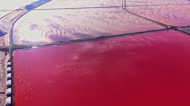 Pembe ve turuncu tonlarla ufku aydınlatarak güneş batarken gökyüzüne karşı çarpıcı bir tezat oluşturan canlı kırmızı tuz düzlükleri arazide yayılıyor..