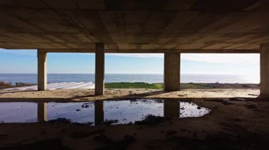 Beton sütunlar, sakin okyanusun nefes kesici manzarasını çerçeveler, mavi gökyüzünü yansıtır ve dokunulmamış doğayı ima eder. Huzurlu bir sahne, derin düşüncelere ve yalnızlığa davetiye çıkarıyor..