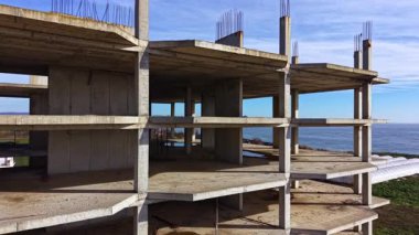 Beton bir yapının inşası deniz tarafından etkileyici bir şekilde yükselir, parlak mavi gökyüzü ve nazik dalgaların oluşturduğu zemine karşı çıplak iskeletini gösterir, ilerlemeyi ve potansiyel potansiyelini gösterir..