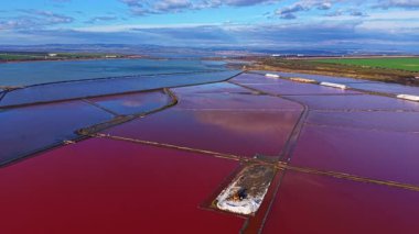 Geniş tuz düzlükleri, parlak bir gökyüzü altında kırmızı ve mavi bir mozaik sergiliyor ve gün boyunca geniş bir alanda çarpıcı bir doğal manzara yaratıyor..
