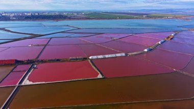 Geniş tuz düzlükleri uzak bir şehrin ufuk çizgisine karşı pembe, mavi ve kahverengi tonlarıyla berrak gökyüzünün altında renkli bir mozaik oluşturur..