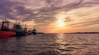 Güneş batarken tekneler yavaşça limanda dinleniyor, sakin suyun üzerinde sıcak bir parıltı saçıyor, alacakaranlıktaki güzel renkleri yansıtıyor ve sakin bir atmosfer yaratıyor..