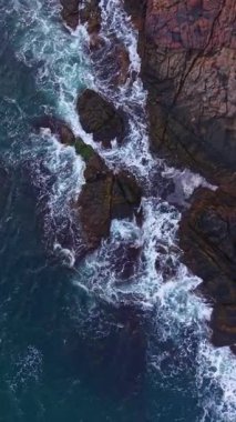 Dalgalanan okyanus dalgaları sivri kayalarla çarpışır ve havaya beyaz köpük gönderir. Güneş, kıyı şeridinin doğal güzelliğini ön plana çıkaran ılık bir parıltı yayar..