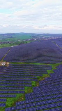 Güneş panelleri kırsal alanda geniş bir alana yayılıyor. Panelleri çevreleyen yeşil alanlar, küçük bir bina ve gri gökyüzünün altında görünen uzak bir kasaba..
