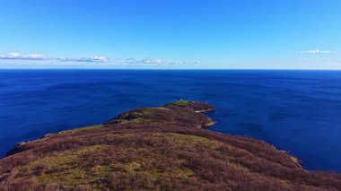Yüksek bir manzara, derin mavi sularla çevrili yeşil bir adayı yakalar. Gökyüzü birkaç bulutla berrak. Bu sahne sahile yakın..