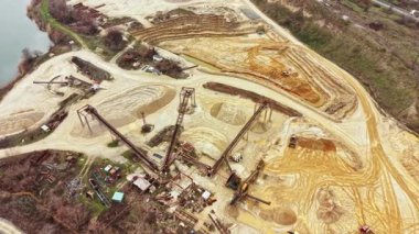 İşçiler ve makineler nehrin kenarındaki bir madende meşguller. Ağır ekipmanlar gün içinde bölgenin çeşitli bölgelerinde toprağı kazıyor ve hareket ettiriyor..