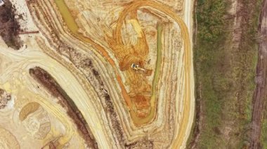 Ağır makineler nehir kenarındaki bir inşaat sahasında çalışıyor, dünyayı hareket ettiriyor ve yeniden şekillendiriyor. Toprak, gün boyunca kırmızı ve kahverengi renkler ve su birikintilerini gösteriyor..