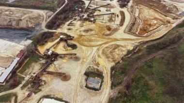 Ağır makineler kırsal bölgedeki bir inşaat alanında çalışıyor. Ekipmanlar toprağı hareket ettiriyor ve toprakta yollar açıyor. Çevresindeki topraklarda ağaçlar ve açık alanlar var..