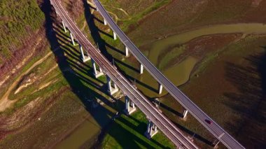 Nehrin üzerinden geçen bir otoyol ve demiryolu köprüsü. Demiryolu boşken araçlar otobanda hareket ediyor. Sahne, su yollarını çevreleyen yeşil araziyi gösteriyor..