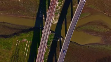 Köprüler su ve kara boyunca uzanır, tren raylarını bir yol ile birleştirir. Bir araç gün boyunca kırsal alanda binaların altında yol boyunca seyahat eder..