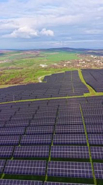 Güneş panelleri kıyıya yakın alanlara yayıldı. Gökyüzünde bulutlar görünen yeşil arazi, bölgeyi çevrelemektedir. Parlak gün ışığı güneş enerjisi kurulumunu vurgular.
