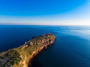 Yukarıdan görünen bir kıyı bölgesi var. Kara berrak mavi suyla okyanusa doğru uzanıyor. Gökyüzü çoğunlukla birkaç bulutla temizdir. Sahne doğayı ve coğrafyayı yakalar..