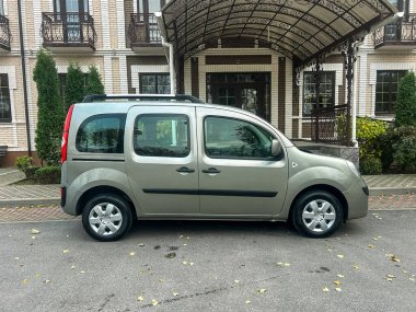 Kapalı girişi olan bir binanın yanında bir araç park halinde. Arazide ağaçlar var. Gündüz vaktidir. Bölge bakımlı ve düzenli görünüyor..