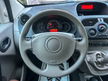 Arabanın içi direksiyonu ve gösterge panelini gösteriyor. Gösterge paneli, araba park halindeyken hız ve yakıt seviyelerini gösteriyor. Pencereden güneş ışığı süzülüyor..