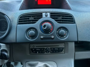 Arabanın içindeki kontrol panelinin yakın görüntüsü. Panelde klima ve radyo düğmeleri gösteriliyor. Güneş ön camdan parlıyor..