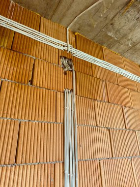 İşçiler gün içinde bir inşaat sahasının duvarına elektrik tesisatı kuruyorlar. Kablolar tuğlalar boyunca düzgünce yerleştirilmiş..