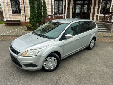 Gümüş bir araba bir binanın önündeki düz bir yüzeye park edilmiştir. Binanın tuğla bir cephesi ve yakınlarda ağaçlar var. Gündüz oldu ve hava açık görünüyor..