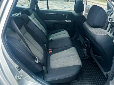 Gümüş renkli bir arabanın arka koltuğu koyu renk ve açık renkli üç koltuğu vardır. Araç gün boyunca şehir manzarası olan bir yere park edilmiş..