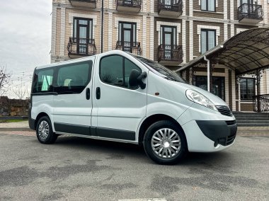 Bulutlu bir günde büyük bir tuğla binanın yanında beyaz bir minibüs park edilir. Minibüs asfalt bir alana yerleştirilmiş ve etrafta kimse yok. Binanın balkonları ve kapalı bir girişi var..