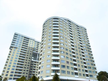 Yoğun bir kentsel alanda gri gökyüzüne karşı yükselen iki uzun yerleşim yeri. Yapılarda çok sayıda balkon ve cam ve beton cephelerin karışımı yer alıyor..