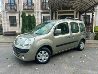 Büyük bir binanın önünde bir araba park edilmiş. Olay yeri, yakınındaki ağaçlar ve kapalı bir girişi olan açık bir günü gösteriyor. Binanın birkaç katı ve penceresi var..