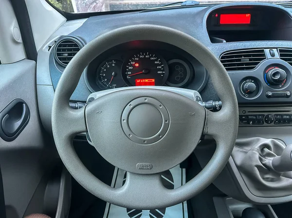 Arabanın içi direksiyonu ve gösterge panelini gösteriyor. Gösterge paneli, araba park halindeyken hız ve yakıt seviyelerini gösteriyor. Pencereden güneş ışığı süzülüyor..